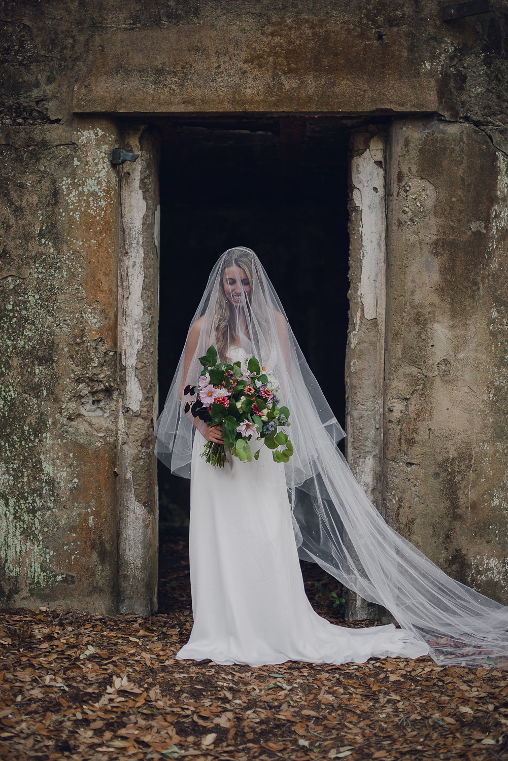 Bride in an elegant gown holding a custom pastel floral bouquet on the beach